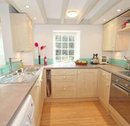 A kitchen with wooden cabinets a sink an oven and a window at White Duck Cottage in Hayle