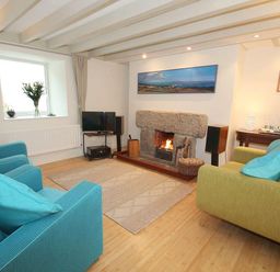 A living room with blue and green chairs a fireplace and a television at White Duck Cottage in Hayle