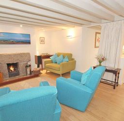 A living room with two blue armchairs and one yellow armchair by a stone fireplace at White Duck Cottage in Hayle