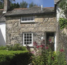 A stone cottage with two windows and a door surrounded by plants and flowers at White Duck Cottage in Hayle