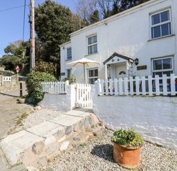 A white house with a white picket fence and stone pathway with potted plants outside at Mallards in Pentewan