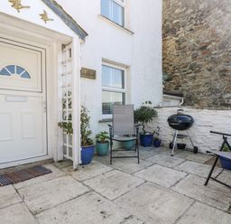 A small outdoor patio area with two chairs a barbecue grill plants in pots and a white door at Mallards in Pentewan