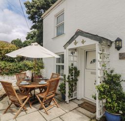 An outdoor patio with a wooden table and four chairs under a white umbrella next to a white house entrance with plants in blue pots at Mallards in Pentewan