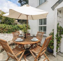 An outdoor patio with a round wooden table and four chairs under a white umbrella at Mallards in Pentewan