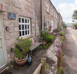 An outdoor view of May Cottage with a bench and flowers in Pentewan
