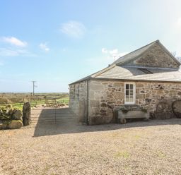 A stone building with old wagon wheels leaning against it and wooden chairs on a gravel area outside at Boar's House in Penzance