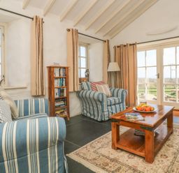 A living room with striped armchairs a wooden coffee table and a bookshelf at Boar's House in Penzance