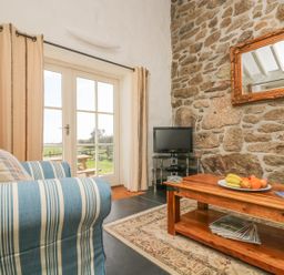 A living room with a striped sofa a wooden coffee table with fruit a TV on a stand and glass doors leading outside at Boar's House in Penzance