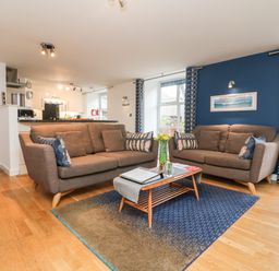 A living room with two brown sofas a coffee table with flowers and books and a blue accent wall at Ebenezer Cottage in Marazion