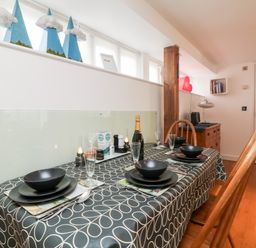 A dining area with a table set for four with black bowls and plates and a bottle on a patterned tablecloth at Ebenezer Cottage in Marazion