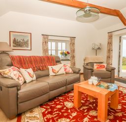 A living room with a leather sofa and armchair a wooden coffee table and open doors showing a garden at Back Of Beyond in St Ives