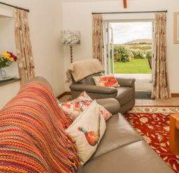 A living room with gray sofas floral cushions and a patterned rug with an open door leading to a garden at Back Of Beyond in St Ives