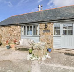 A stone and wood house exterior with a bench and flower pots at Back Of Beyond in St Ives
