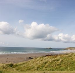 A beach with people on the sand and grassy dunes in the foreground with an ocean and cloudy sky at Angarrack Farmhouse in Hayle