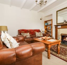 A living room with brown leather sofas a wooden coffee table a lit fireplace a patterned rug and a wooden bookshelf at Angarrack Farmhouse in Hayle