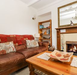 A living room with a brown leather sofa red and beige cushions wooden coffee table and a fireplace with a mirror at Angarrack Farmhouse in Hayle