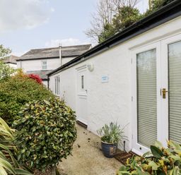 The exterior side view of a white building with plants and shrubs along a concrete pathway at Godrevy Barn in Hayle