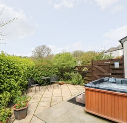 An outdoor patio area with a hot tub black metal chairs and table surrounded by green bushes at Godrevy Barn in Hayle