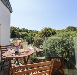 A balcony with wooden table and chairs glass railing flowers in vase and greenery outside at Little Hamlin in Rilla Mill Nr Callington