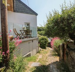 A garden path beside a house with a balcony with a table and chairs and flowering plants at Little Hamlin in Rilla Mill Nr Callington