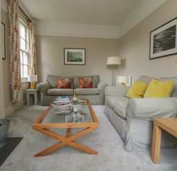 A living room with two sofas a glass coffee table and framed pictures on the walls at Penwarne Lodge in Mawnan Smith