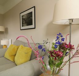 A living room with a grey sofa with yellow cushions a vase of flowers and two lamps at Penwarne Lodge in Mawnan Smith