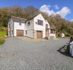 A house with garages and windows surrounded by gravel driveway and trees at Carne Mill in Manaccan
