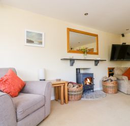 A living room with armchairs a wood-burning stove and a wall-mounted television at Carne Mill in Manaccan