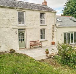 A white stone house with green door and windows garden patio bench and potted plants at Little Chycoose in Truro