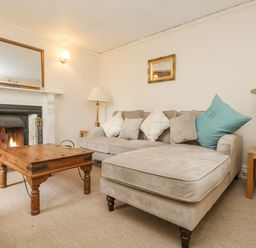 A living room with a beige sectional sofa a wooden coffee table and a fireplace at Little Chycoose in Truro