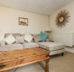 A living room with a beige sofa cushions wooden coffee table lamps and a decorative mirror at Little Chycoose in Truro
