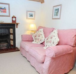 A living room with a pink sofa near a fireplace and a lamp at Rose Cottage Manaccan