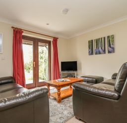 A living room with leather sofas a wooden coffee table and a television near glass doors with red curtains at Cuckoo's Cottage in Falmouth
