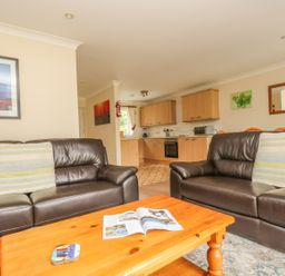 A living room with two brown leather sofas and a wooden coffee table with a magazine on it next to a kitchen with wooden cabinets at Cuckoo's Cottage in Falmouth