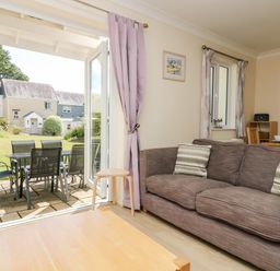 A living room with a brown sofa and striped cushions next to open glass doors leading to a patio with a black table and chairs at Trelease in Falmouth