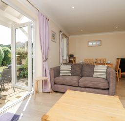 A living room with a brown sofa and wooden coffee table next to an open glass door leading to a garden at Trealse in Falmouth