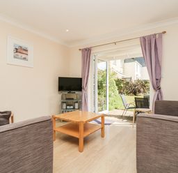 A living room with brown sofas a wooden coffee table and a TV on a metal stand next to open doors leading to a garden at Trelease in Falmouth
