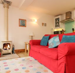 A living room with a red sofa blue cushions a fireplace and a polka dot rug at Plum Cottage in Colebrooke near Crediton