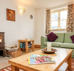 A living room with a wood-burning stove sofa with purple cushions wooden tables and a window at Apple Cottage Colebrooke near Crediton