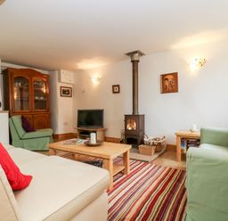 A living room with a wood burning stove a television a wooden cabinet sofa and armchairs at Apple Cottage in Colebrooke near Crediton