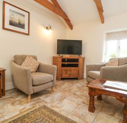 A sitting area with two armchairs a wooden TV stand with a television a wooden side table and a framed picture on the wall at Roosters in Lostwithiel