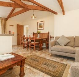 A living room with a dining table wooden chairs a beige sofa and a wooden coffee table at Roosters in Lostwithiel