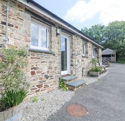 An exterior view of a stone building with white doors and windows gravel and asphalt ground with plants in wooden barrels at Byre Lostwithiel