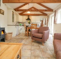 A kitchen and dining area with wooden beams on the ceiling and armchairs near a wood stove at Byre Lostwithiel