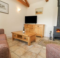 A living room with a wood stove and wooden furniture including a coffee table and sideboard at Byre in Lostwithiel