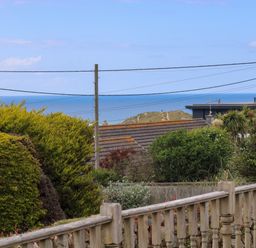 A garden with bushes and a wooden fence overlooking rooftops and the sea at Bethany Bay View in Holywell Bay