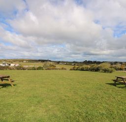 A grassy field with two wooden picnic tables and a cloudy sky at Mynheer Farm Barn Nr Portreath