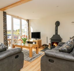 A living room with two gray sofas a wooden coffee table with flowers a television and a wood burning stove at Mynheer Farm Barn Nr Portreath