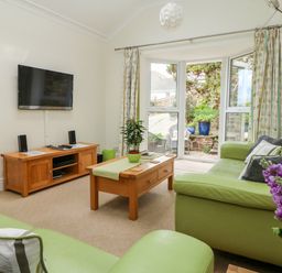 A living room with green sofas a wooden coffee table a wooden TV stand and a wall mounted TV at Seabien in Falmouth