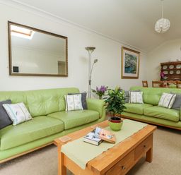 A living room with two green sofas a wooden coffee table with books and a plant a dining table in the background at Seabien in Falmouth